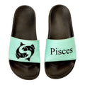 Pair of black slides with 'Pisces' and a zodiac symbol on a light green strap against a white background